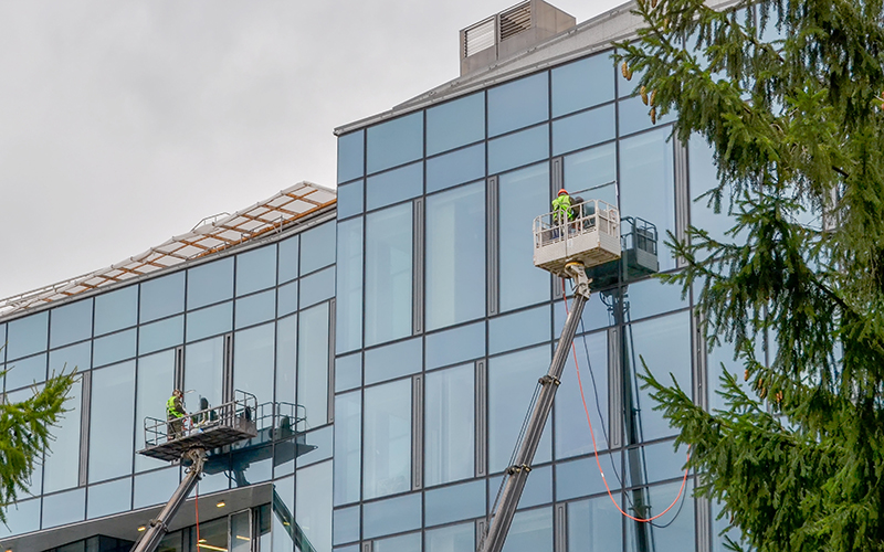 Two workers in overalls on an elevator washes the glass wall of a building.